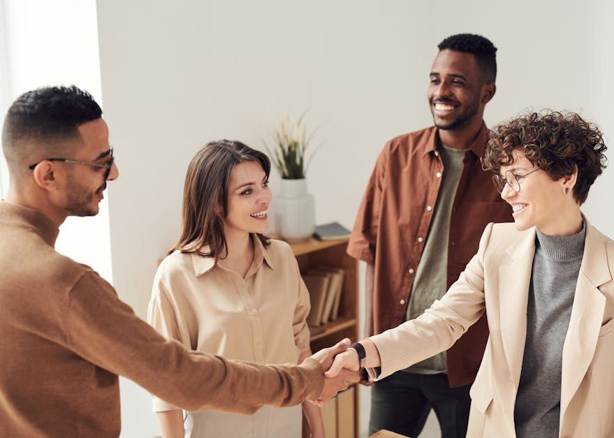 Four colleagues smiling and shaking hands in a bright office setting.