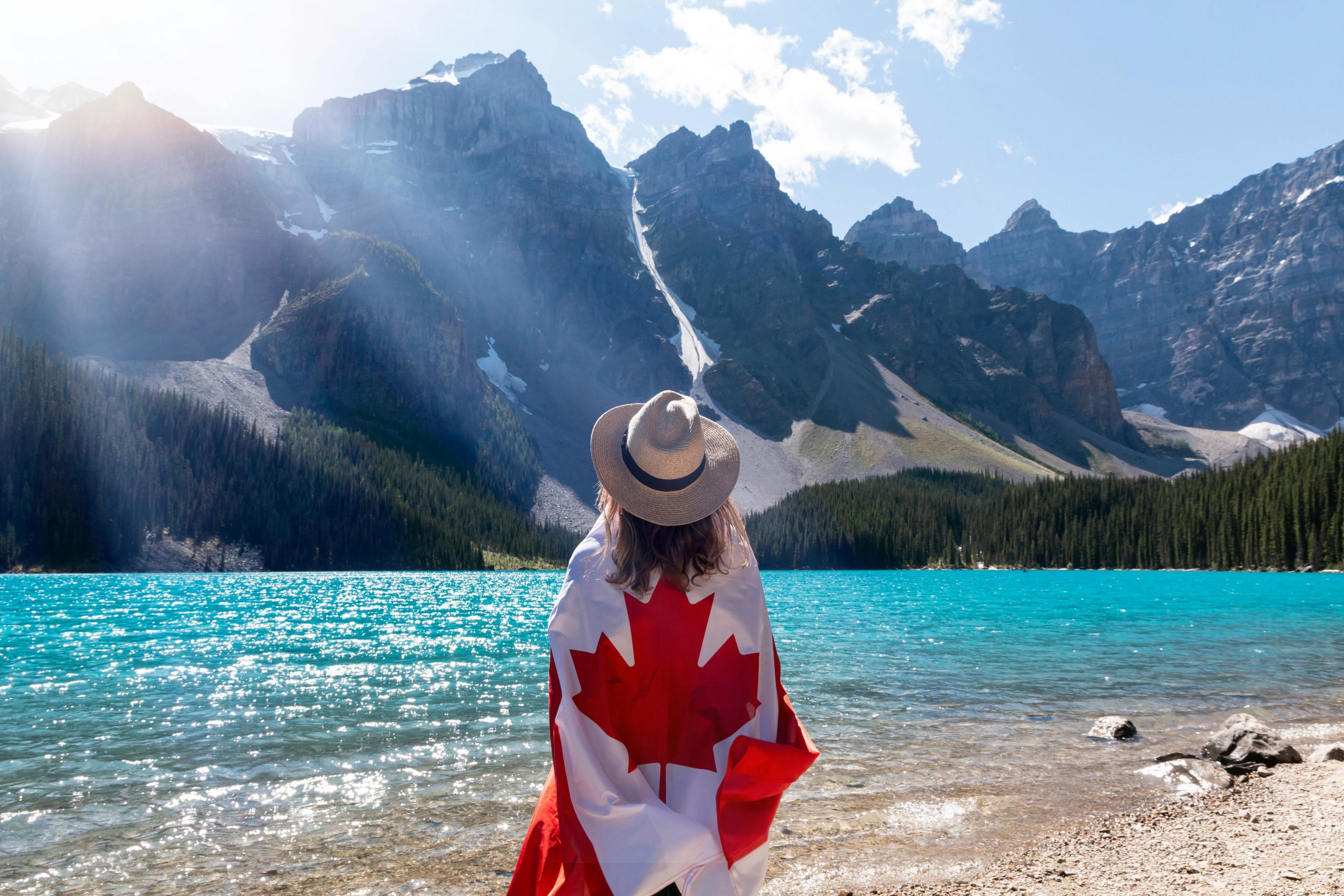 A person in a hat wrapped in a Canadian flag overlooks Moraine Lake and mountains.